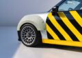 Close-up of a car’s front left side with a fiberglass fender, multi-spoke alloy wheel, and black and yellow diagonal stripes—a nod to MINI’s Rally DNA Gets a Deus Makeover in Two Radical JCW Builds.