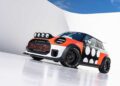 A customized Mini Cooper, inspired by MINI’s Rally DNA Gets a Deus Makeover in Two Radical JCW Builds, features rally lights, wide fenders, and a black-and-white polka dot design, parked on a reflective white surface beneath a blue sky.