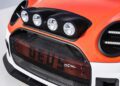 Close-up of the front of an orange and white car, showcasing four round headlights above the grille and a mesh grille with visible red components behind it—capturing MINI’s Rally DNA Gets a Deus Makeover in Two Radical JCW Builds.