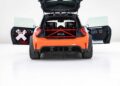 Rear view of an orange car with both side doors and rear hatch open, showcasing a roll cage and racing interior—a scene where MINI’s Rally DNA gets a Deus makeover in one of two radical JCW builds, all set in a white studio.