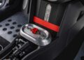 Close-up of a car's center console showing metallic toggle switches with a red safety cover, black and metal detailing, and a section of the footwell—capturing MINI’s Rally DNA Gets a Deus Makeover in Two Radical JCW Builds.