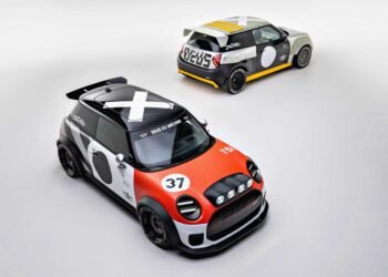 Two modified Mini Coopers, showcasing MINI’s Rally DNA with a Deus makeover, are parked on a plain white surface—one in striking orange and black, the other in bold gray and yellow.