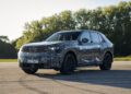 A camouflaged BMW iX5 Hydrogen test vehicle is parked on an open paved area with trees in the background, hinting at the brand's commitment to future series production of hydrogen-powered models.