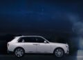 A white Rolls-Royce Cullinan luxury SUV parked outdoors at night under a starry sky, shown in side profile view, echoes elegance with its signature Starlight Headliner illuminating the interior.