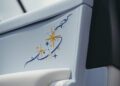 Close-up of a light blue leather Rolls-Royce Cullinan car seat featuring embroidered gold, blue, and white stars and swirling lines in a cosmos-inspired decorative pattern, reminiscent of the iconic Starlight Headliner.