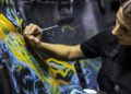 A person in a black apron paints abstract yellow and blue patterns on a canvas, inspired by the swirling beauty of the cosmos and the shimmer of a Starlight Headliner.