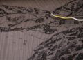 Black textured surface featuring subtle engraved buildings and landscape; a thin yellow and white cable runs across the upper right corner.