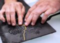 Close-up of hands touching a tactile map with raised lines and textured surfaces, designed for visually impaired users.