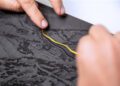 Close-up of hands tracing a yellow line on a textured, black-and-gray map or surface with raised details.