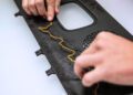 Two hands are placing a yellow wire or cord along a designated groove on a black plastic panel with a circular vent.