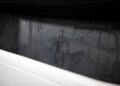 Close-up of a car interior panel featuring intricate woodwork with an engraved image of a vintage automobile and palm trees, evoking the timeless elegance of a Rolls-Royce.