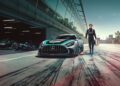 A race car driver in a Mercedes-AMG suit stands next to a limited edition Mercedes-AMG GT2 Edition sports car on a racetrack, with another race car visible in the garage behind him.