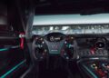 View of a Mercedes-AMG GT2 race car cockpit showing the steering wheel with multiple buttons, a dashboard, and various controls, with a racetrack visible through the windshield.