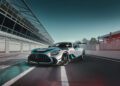 A silver Mercedes-AMG GT2 Edition sports car with turquoise accents is parked on a racetrack next to a pit lane under a clear sky.