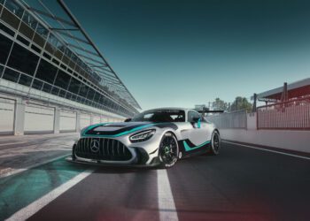 A silver Mercedes-AMG GT2 Edition sports car with turquoise accents is parked on a racetrack next to a pit lane under a clear sky.