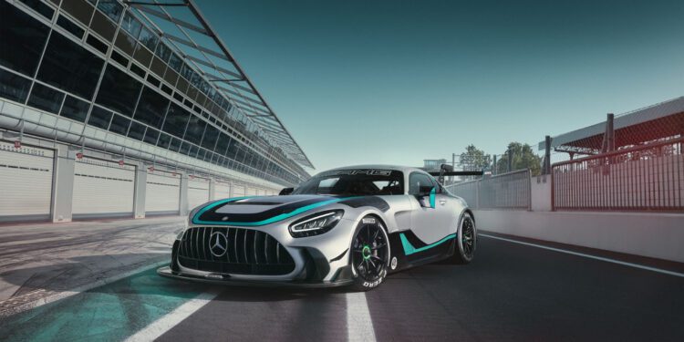 A silver Mercedes-AMG GT2 Edition sports car with turquoise accents is parked on a racetrack next to a pit lane under a clear sky.