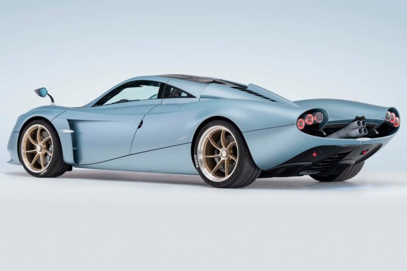 A matte blue sports car with gold wheels, four circular rear lights, and a sleek aerodynamic design—reminiscent of those seen when Pagani plans to showcase four hypercar icons at the upcoming 9th Historic Minardi Day in Imola. Photographed from a rear-side angle.
