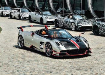 A silver and black sports car with red accents is parked on a cobblestone driveway, surrounded by similar cars—possibly stars like those Pagani will showcase at the upcoming 9th Historic Minardi Day in Imola.
