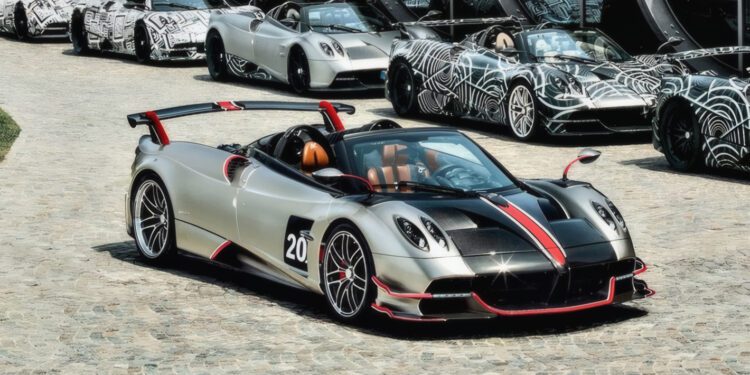 A silver and black sports car with red accents is parked on a cobblestone driveway, surrounded by similar cars—possibly stars like those Pagani will showcase at the upcoming 9th Historic Minardi Day in Imola.