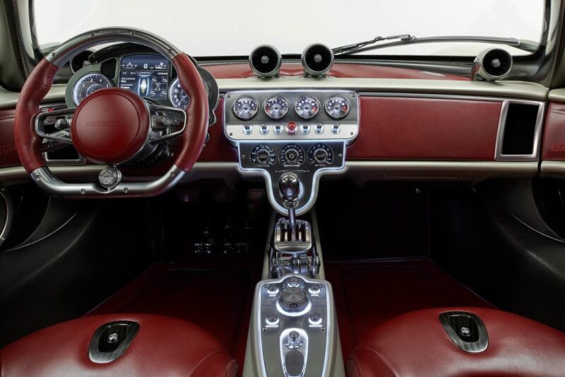 Red and silver luxury car interior featuring a leather-wrapped steering wheel, central gauges, control buttons, and an advanced digital display—reminiscent of Pagani to Showcase Four Hypercar Icons at the Upcoming 9th Historic Minardi Day in Imola.