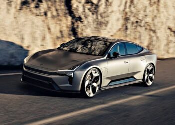 A sleek, silver electric sedan with aerodynamic lines—possibly the Polestar 5, which debuts at IAA 2025 as the brand’s first true flagship EV GT—drives along a road beside a rocky wall.
