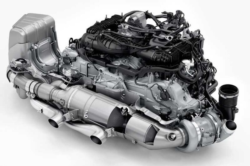 A complex, modern automotive engine with various pipes, cables, and metallic components is showcased on a white background—reminiscent of the cutting-edge powertrain in the Review: 2025 Porsche 911 Carrera GTS T-Hybrid Electrifies Potent Performance.