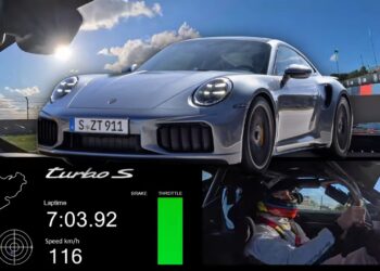 A silver Porsche 911 Turbo S on a racetrack with lap time, speed, and throttle data displayed, showcasing how the 992.2 Turbo S is 14 seconds quicker than before at the 'Ring; a driver in racing gear commands the wheel.