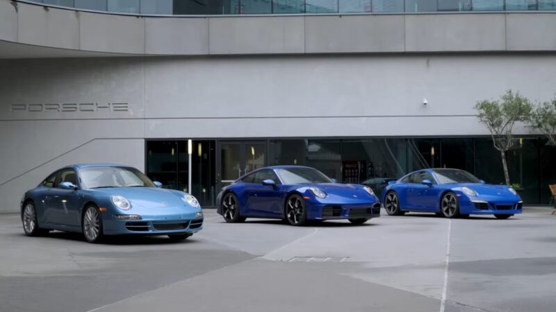 Three blue Porsche sports cars of different models are parked outside a modern Porsche dealership building, reflecting the legacy and strong community spirit celebrated by the Porsche Club of America.