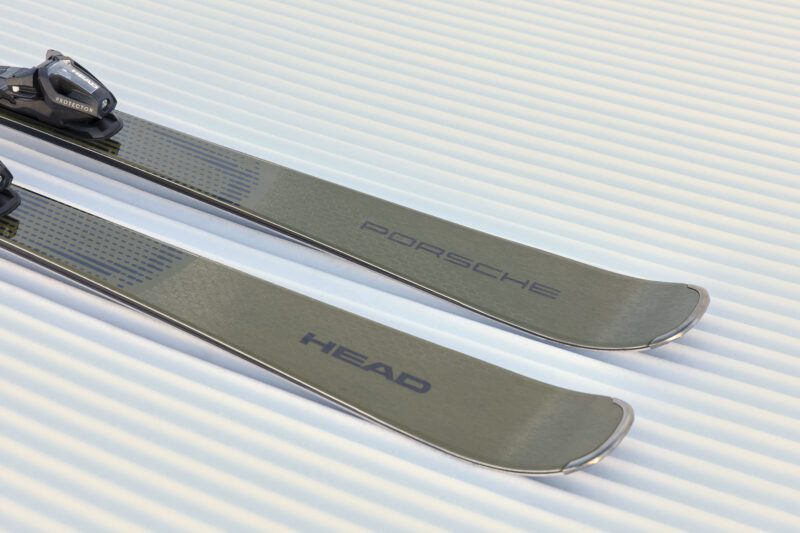Close-up of two skis from the ski collection, lying on grooved snow, with "Porsche" and "HEAD" branding visible on their surfaces.