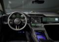 Modern car interior featuring a digital dashboard, large touchscreen displays, navigation system, and illuminated ambient lighting, with a Porsche logo on the steering wheel.