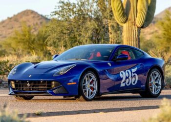 A blue Ferrari F12berlinetta, a true example of Ferrari supercars, with the number 235 on the door, is parked on a road in a desert landscape surrounded by cacti and mountains.