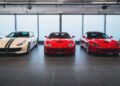 Three sports cars—two red and one white with black stripes—are parked side by side in a showroom with large windows, ready to impress at the upcoming RM Sotheby’s Zurich auction featuring top-tier hypercars.