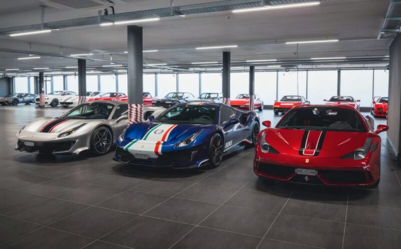 Three Ferrari hypercars are parked side by side in a modern indoor showroom, surrounded by other luxury vehicles. This striking lineup could be the highlight of an RM Sotheby’s Zurich auction.
