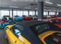 A showroom in Zurich, Switzerland displays various luxury sports cars and hypercars, including models in yellow, blue, red, and green, lined up in a well-lit room; photo dated October 2025 during the Zurich auction by RM Sotheby’s.