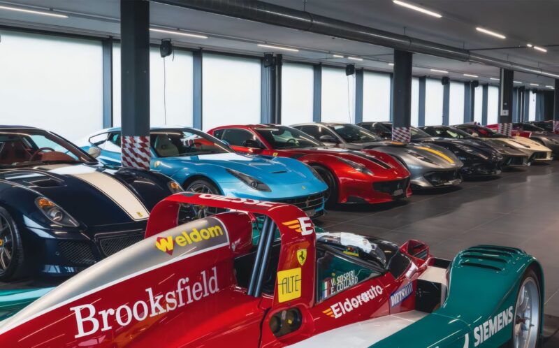 Several high-end sports cars, including hypercars like a Formula 1 car and multiple Ferraris, are parked in a brightly lit indoor showroom at the upcoming RM Sotheby’s Zurich auction.