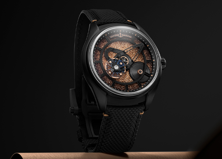 A luxury wristwatch with a black case, textured black strap, and a detailed skeleton dial featuring gold accents and visible mechanical components, the Freak X Crystalium by Ulysse Nardin is a striking limited edition against a dark background.