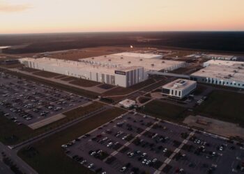 Aerial view of the Volvo South Carolina plant, showcasing multiple buildings, a main entrance, and parking lots filled with cars at sunset—home of the next-gen hybrid XC60.