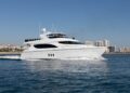 A large white luxury yacht cruises on blue water with a city skyline and tall buildings in the background under a clear sky, offering an unforgettable maritime experience.