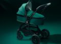 A dark green and black Aston Martin stroller with a bassinet attachment is positioned on a matching dark green background—perfect for next generation car lovers.
