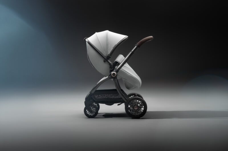 A modern baby stroller with a white canopy and seat, black frame, and large wheels—perfect for car lovers seeking next generation style—positioned against a dark gradient background.