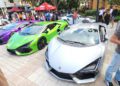 Three Lamborghini sports cars—purple, green, and silver—are parked side by side at an outdoor car event with people gathered around.