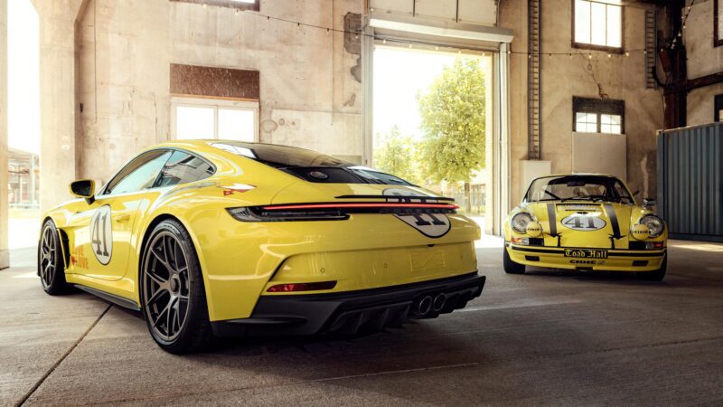 Two yellow Porsche 911 S/T legends with racing numbers are parked inside a spacious, sunlit industrial garage.