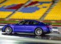 A blue Porsche Taycan Turbo GT drives quickly on a track at Sydney Dragway, with colorful empty stadium seats in the background.