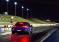 A blue Porsche Taycan Turbo GT is positioned at the starting line of Sydney Dragway at night, illuminated by overhead lights and the glow of its rear lights, ready to chase a quarter-mile record.