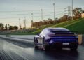A blue Porsche Taycan Turbo GT is positioned on the Sydney Dragway, ready to accelerate down the quarter-mile, with green grass and stadium lights in the background.