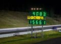 A drag racing scoreboard at Sydney Dragway displays times of 9.08 and 15.66 seconds at night, with a blue Porsche Taycan Turbo GT on the track in the background chasing a quarter-mile record.