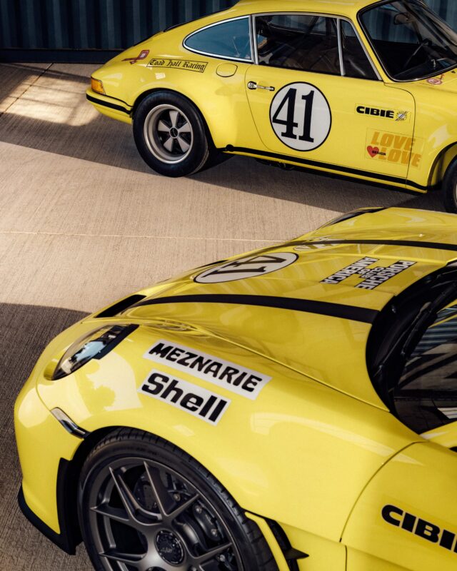 Two yellow Porsche 911 S/T race cars with black wheels and sponsor decals, including Shell and Cibie, are parked side by side on a concrete surface—true legends of racing history.