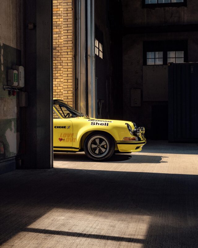 A yellow Porsche 911 S/T, a true legend, is partially visible through an open garage door, sunlight highlighting its front end and racing decals.