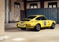 A yellow vintage Porsche 911 S/T race car, a true legend with number 41, is parked inside an industrial building near a blue shipping container.