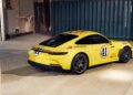 A yellow Porsche 911 S/T sports car with the number 41 and racing decals is parked indoors near a blue shipping container—a true legend among performance vehicles.
